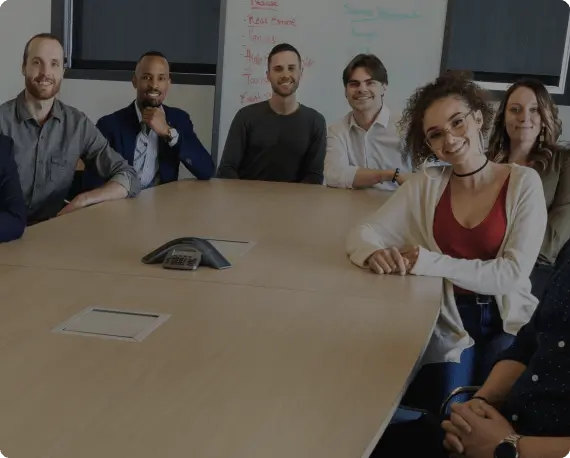 A group of professionals smiling and sitting around a conference table, representing teamwork and collaboration at Red Sun IT Services.